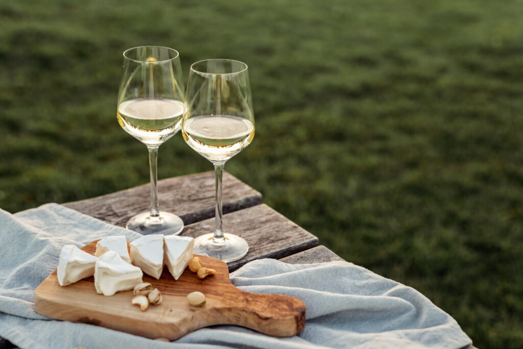 Two glasses of white wine and wooden plate with cheese and nuts